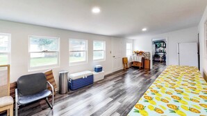 Una habitación amplia con suelo de madera, un ventanal grande, una silla, una mesita y una estantería.