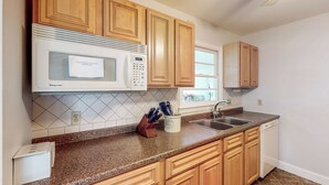 Una cocina con armarios de madera, microondas, fregadero y lavavajillas.