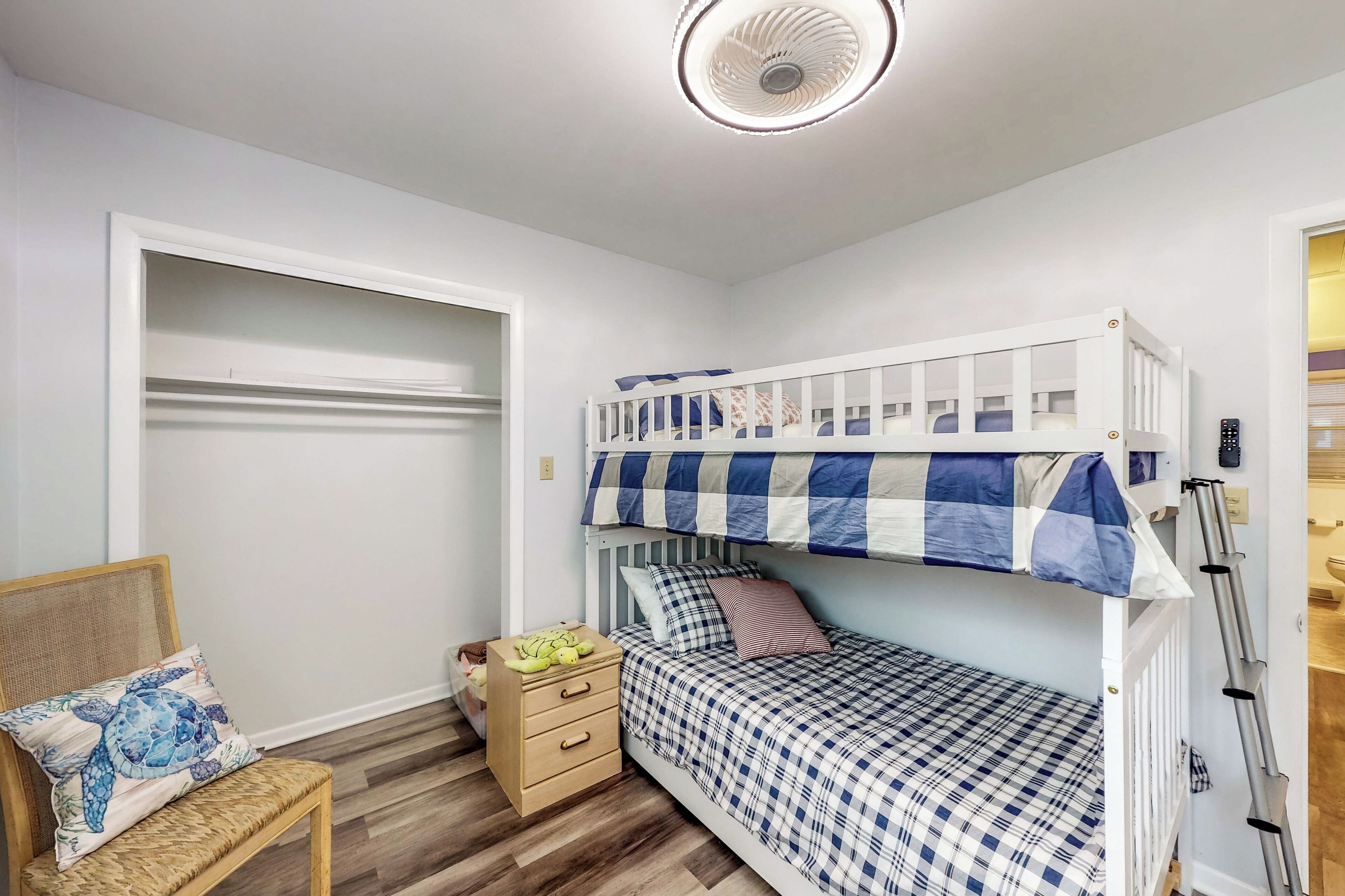 A bedroom with a bunk bed, a wooden nightstand with drawers, a wicker chair, and a ceiling fan.