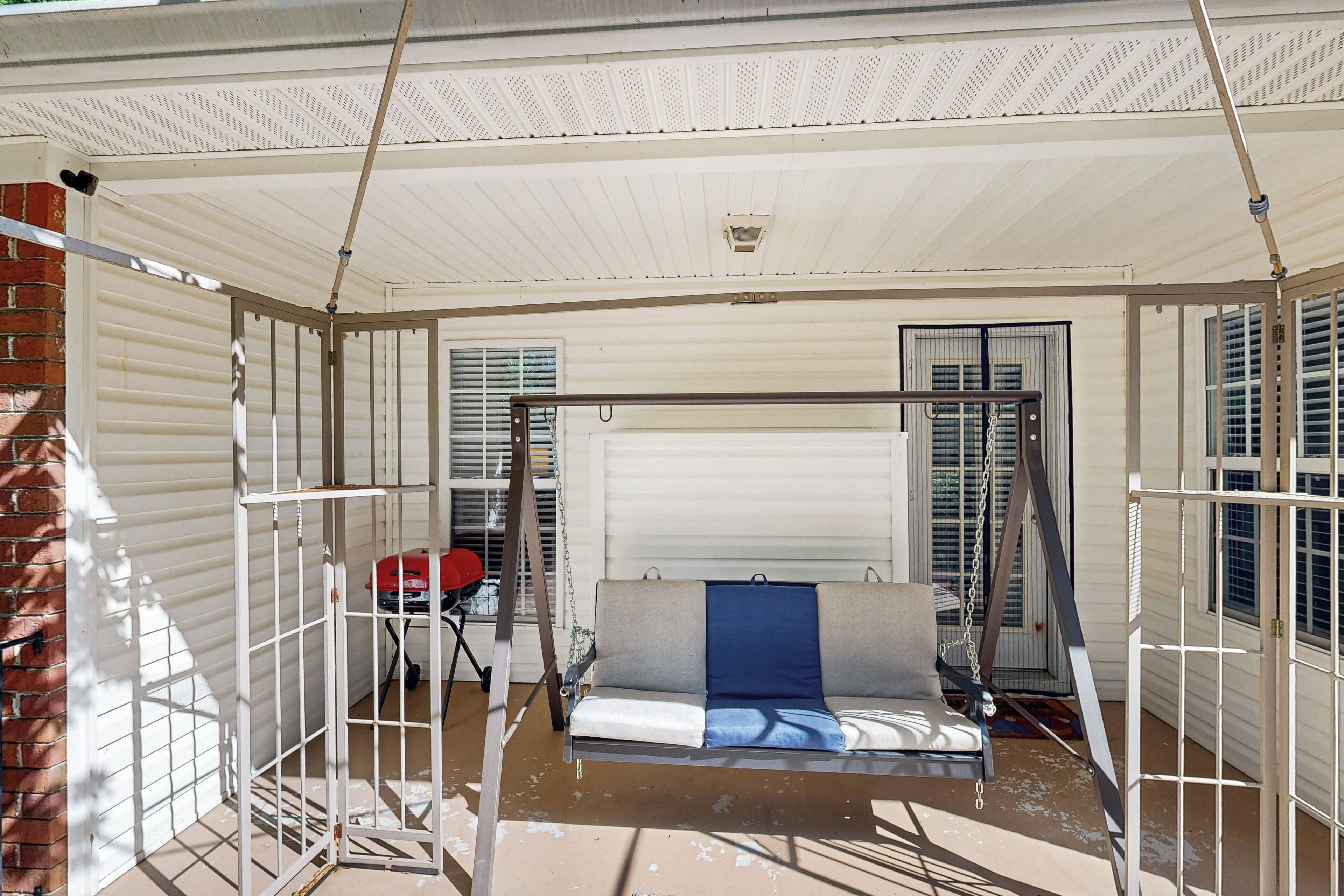 A covered outdoor area with a swing set, a sofa, and a brick wall.