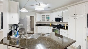 Une cuisine moderne avec des meubles blancs, un plan de travail en granit, un îlot central et un luminaire suspendu.