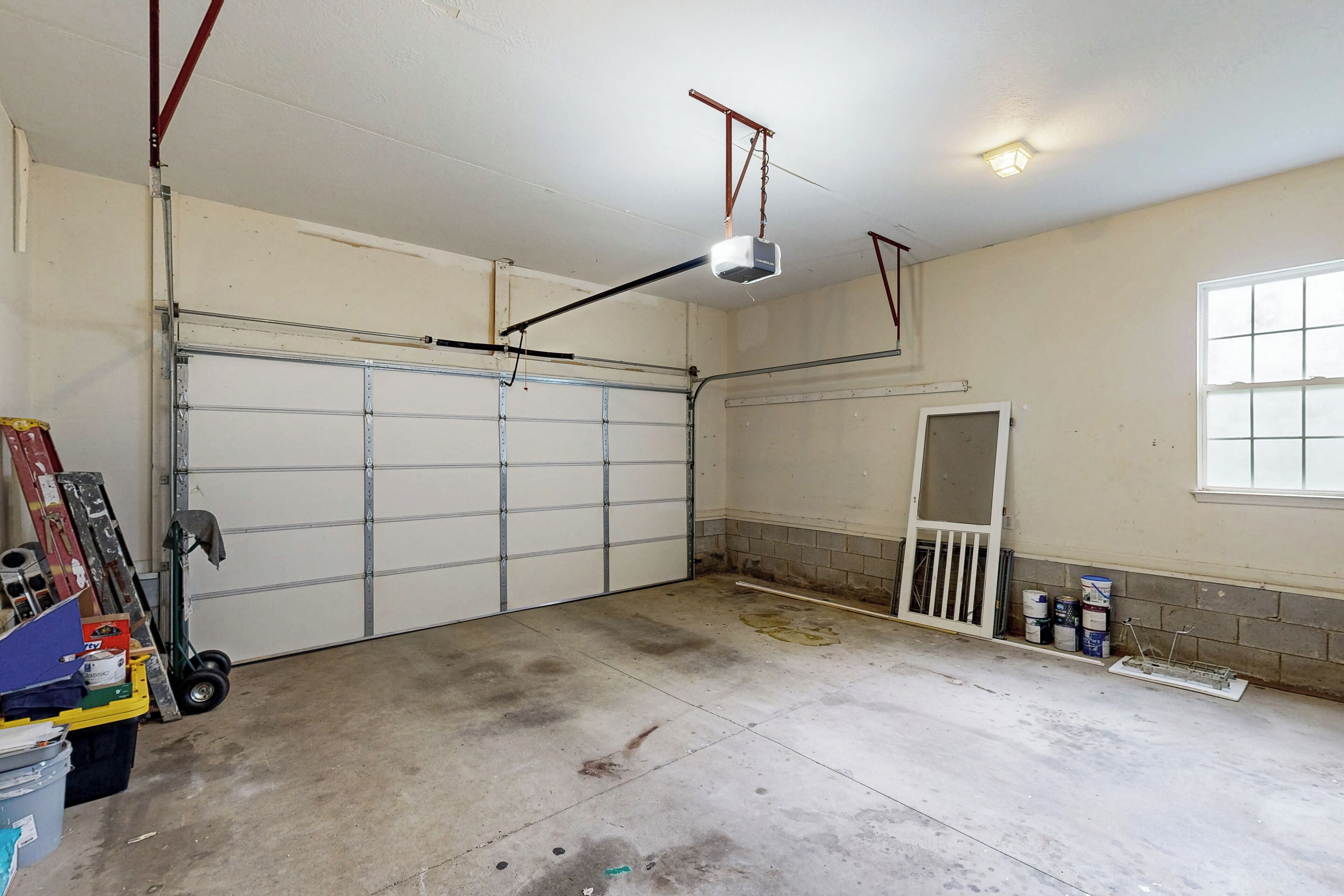 A garage with a closed garage door, a ceiling-mounted projector, and a window on the right wall.