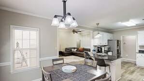 Une cuisine moderne dotée d’un îlot central, un coin repas avec une table et des chaises, et un salon avec un canapé et un ventilateur de plafond.