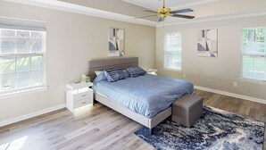 Une chambre à coucher avec un lit, des tables de chevet, un ventilateur de plafond et des œuvres d’art accrochées aux murs.