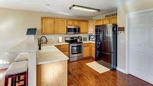 A modern kitchen with wooden cabinets, stainless steel appliances, and a bar area with stools. - 4 Mi to Memorial Stadium: Family Escape in Lincoln (Lincoln)