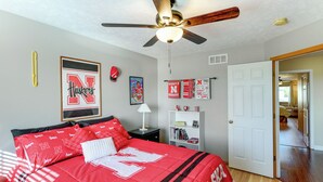 A bedroom with a red bedspread, a ceiling fan, and a bookshelf. - 4 Mi to Memorial Stadium: Family Escape in Lincoln (Lincoln)