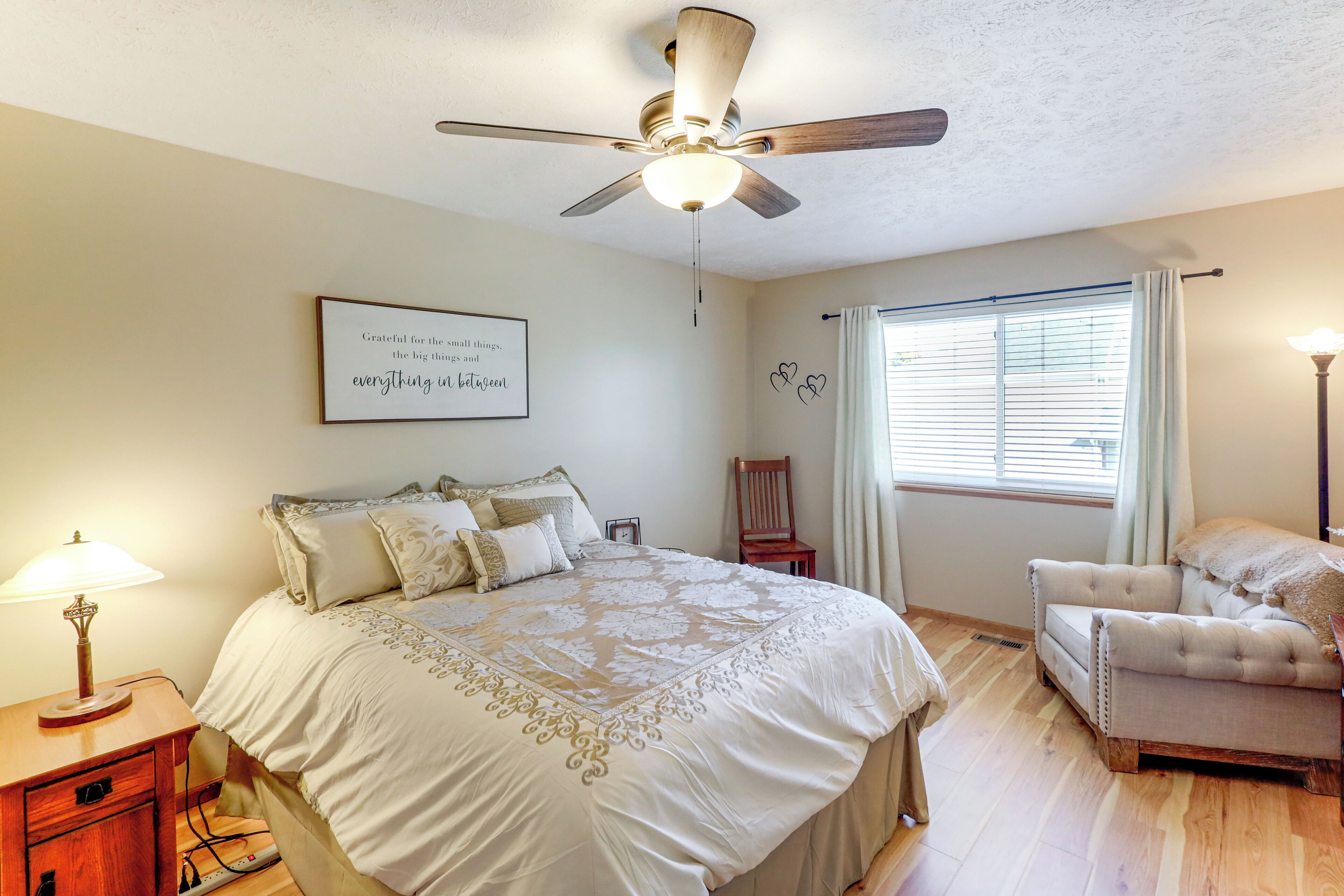 A bedroom with a bed, a chair, a desk, a ceiling fan, and a window with curtains.