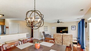 A dining area with a wooden table, chairs, a chandelier, and a television in the background. - 4 Mi to Memorial Stadium: Family Escape in Lincoln (Lincoln)