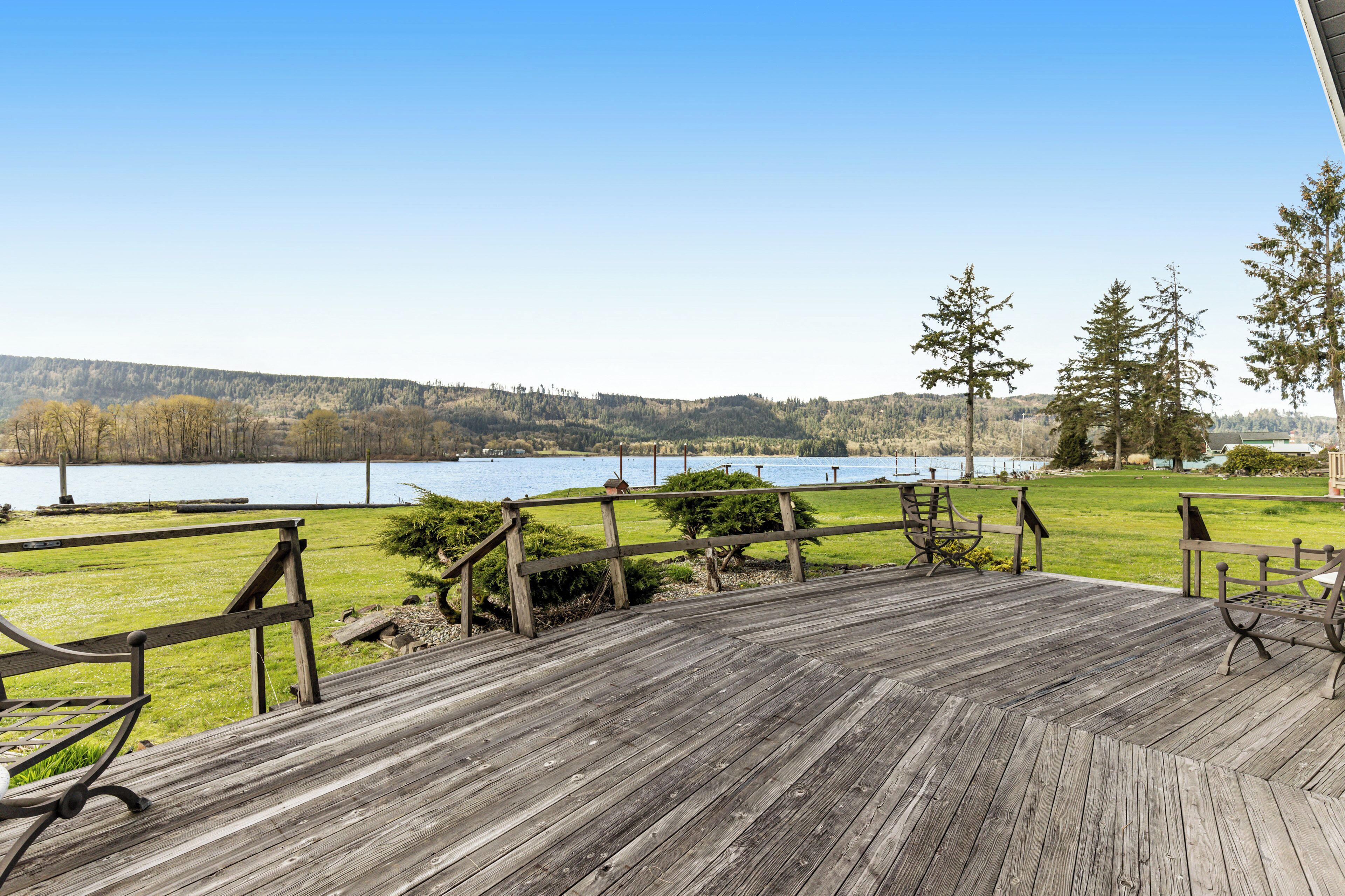 A wooden deck with benches overlooking a lake, surrounded by trees and hills.