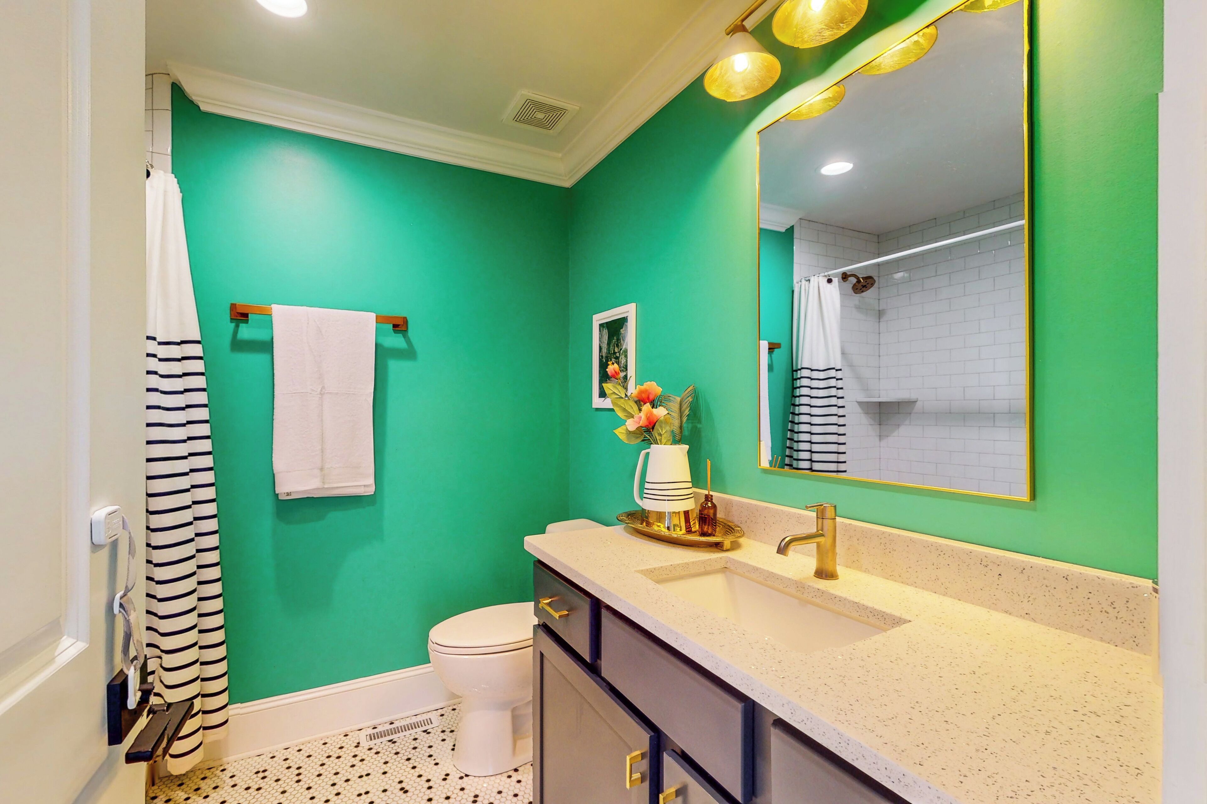 A bathroom with a green wall, a white toilet, a striped shower curtain, a sink with a gold faucet, and a mirror with a gold frame.