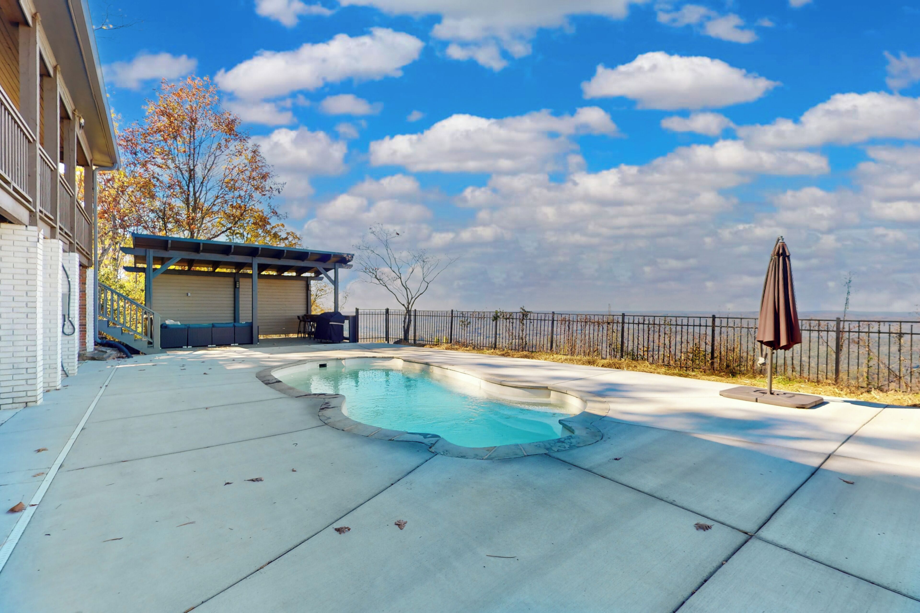 Una piscina con un porche cubierto, un patio cercado y un edificio con garaje.