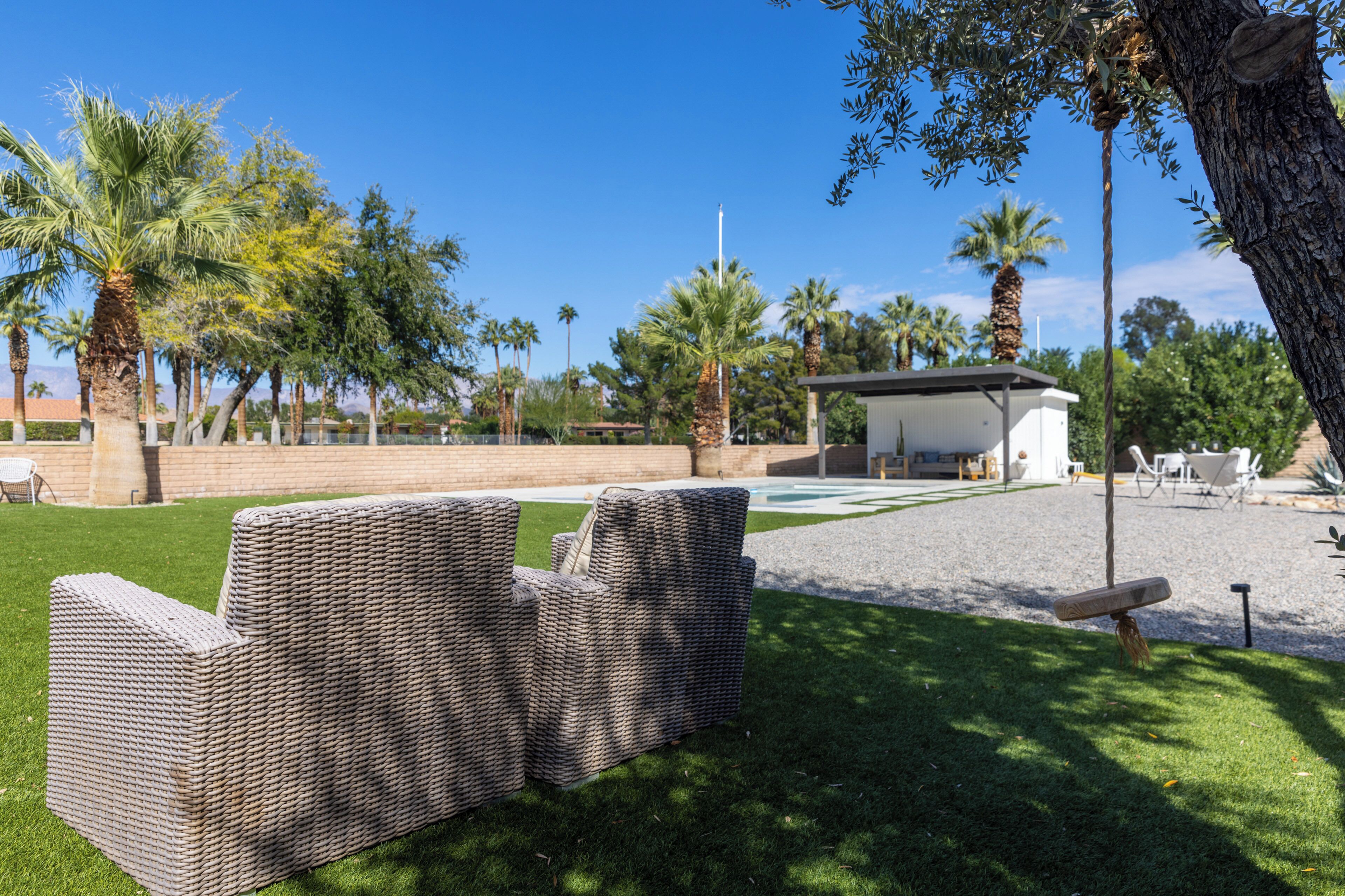 A patio area with wicker furniture, a pool, and palm trees.