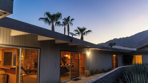 A modern house with a patio, a stone fireplace, and a view of palm trees and mountains. - 3BR Designer Hideaway w/ Private Pool, spa (Borrego Springs)
