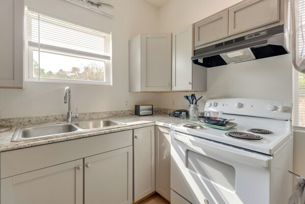 A kitchen with a double sink, white cabinets, a stove, and a window with blinds. - 4 Mi to Lake Bastrop: Pet-friendly Apartment! (Bastrop)