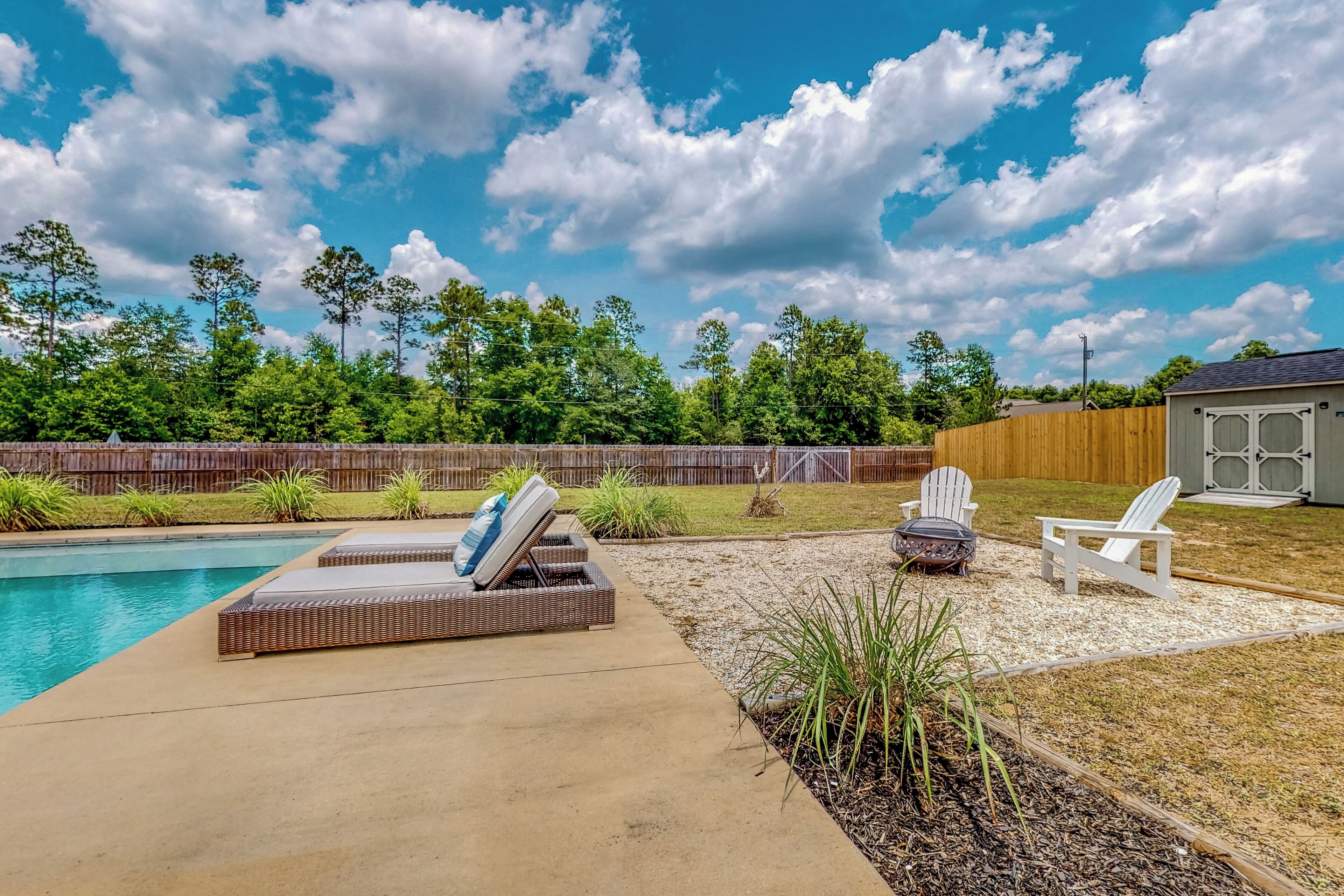 A backyard with a swimming pool, lounge chairs, and a wooden deck.