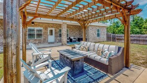A covered patio with a wooden pergola, outdoor seating, and a stone table. - 4BR Retreat w/ a Saltwater Pool & Fire Table (Crestview)