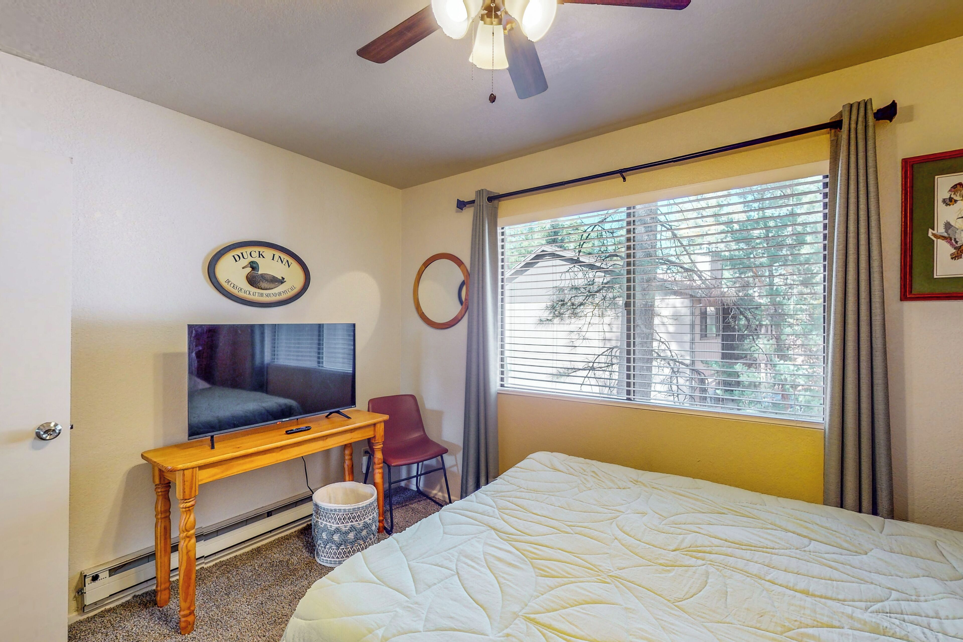 A hotel room with a bed, a TV, a desk, and a window with blinds.
