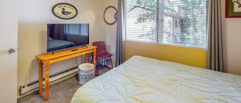 A hotel room with a bed, a TV, a desk, and a window with blinds.
