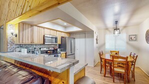 Una cocina moderna con armarios de madera, una isla central y una zona de comedor con mesa y sillas de madera.