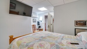 Un dormitorio con cama, una silla, un escritorio y un televisor montado en la pared.