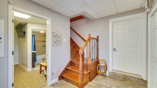 Una escalera de madera con barandilla, una puerta blanca y un pasillo que conduce a un baño con cortina de ducha azul.