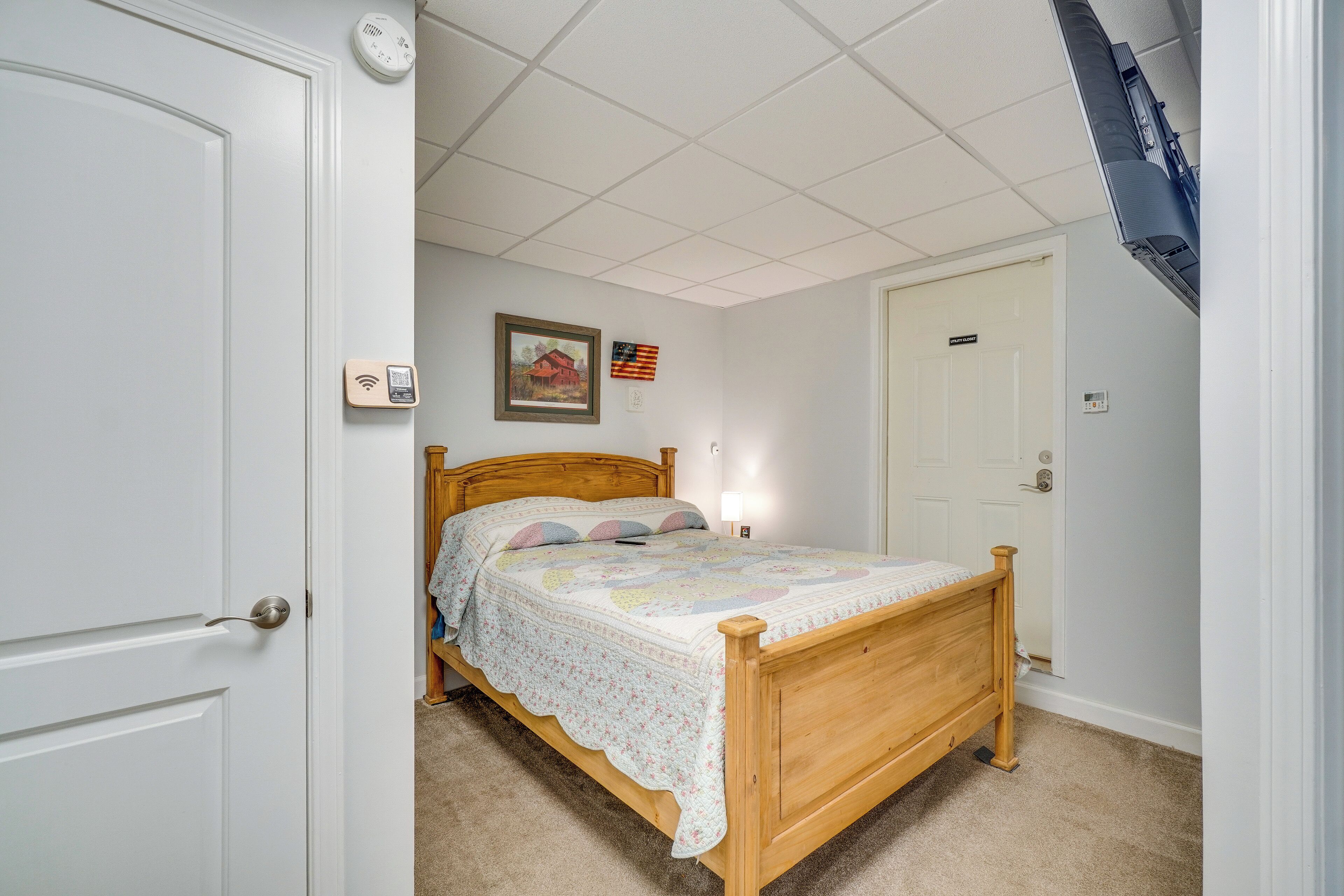 A bedroom with a wooden bed, a white door, a thermostat, and a framed picture on the wall.