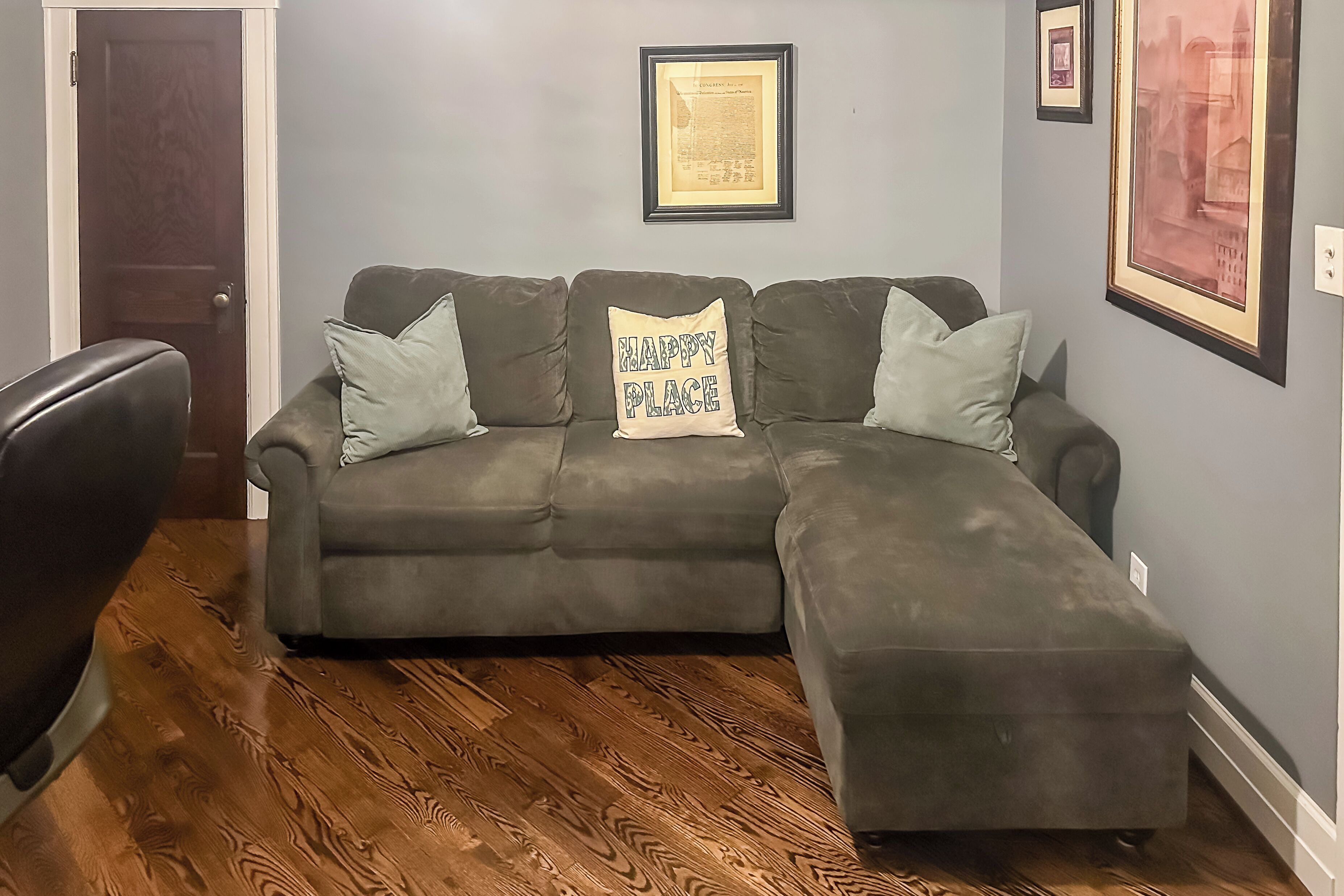 A living room with a sectional sofa, a wooden floor, and framed artwork on the walls.