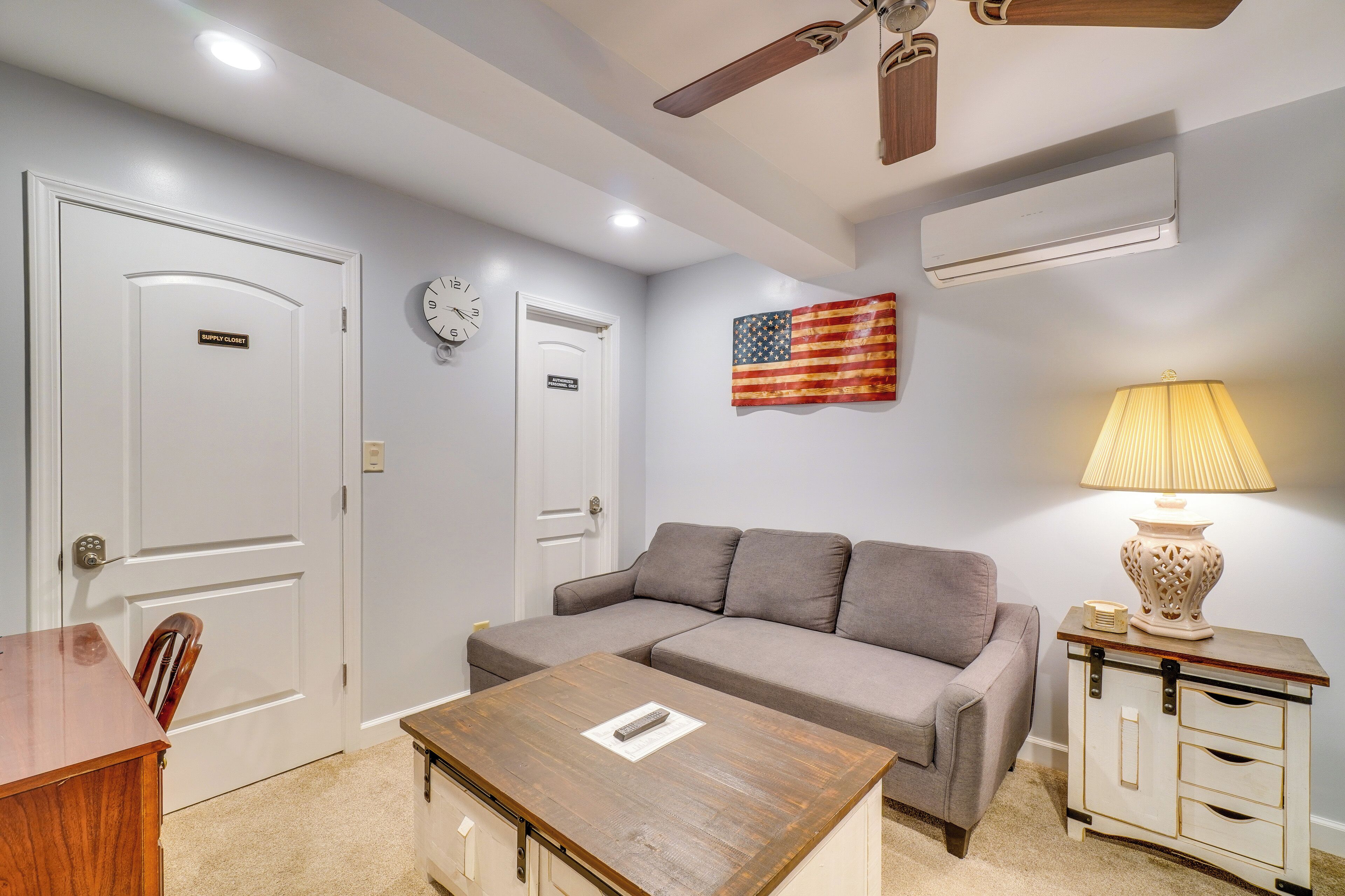 A room with a gray sofa, a wooden table, a lamp, and an American flag.