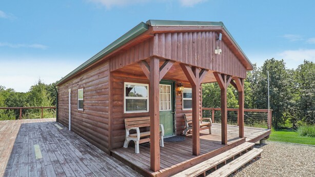 A wooden cabin with a porch, a bench, and a door. - Fishing Pond & Treehouse: Tranquil Maysville Cabin (Maysville)
