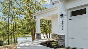 A house with a white garage, stone pillars, and a view of a lake. - 3BR Riverfront Home w/ Kayaks & Game Room (Seaford)