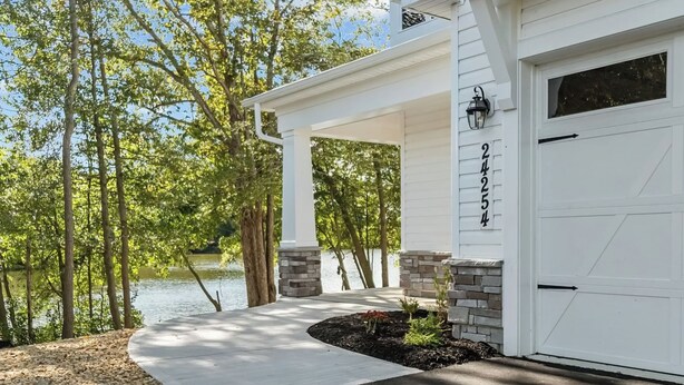 A house with a white garage, stone pillars, and a view of a lake. - 3BR Riverfront Home w/ Kayaks & Game Room (Seaford)