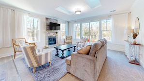 A spacious living room with a fireplace, large windows, and a ceiling fan. - 3BR Riverfront Home w/ Kayaks & Game Room (Seaford)