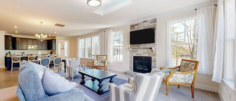A spacious living room with a fireplace, a dining area, and a kitchen in the background.