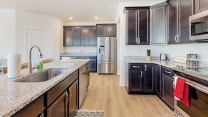 A modern kitchen with dark cabinets, stainless steel appliances, and granite countertops. - 3BR Riverfront Home w/ Kayaks & Game Room (Seaford)