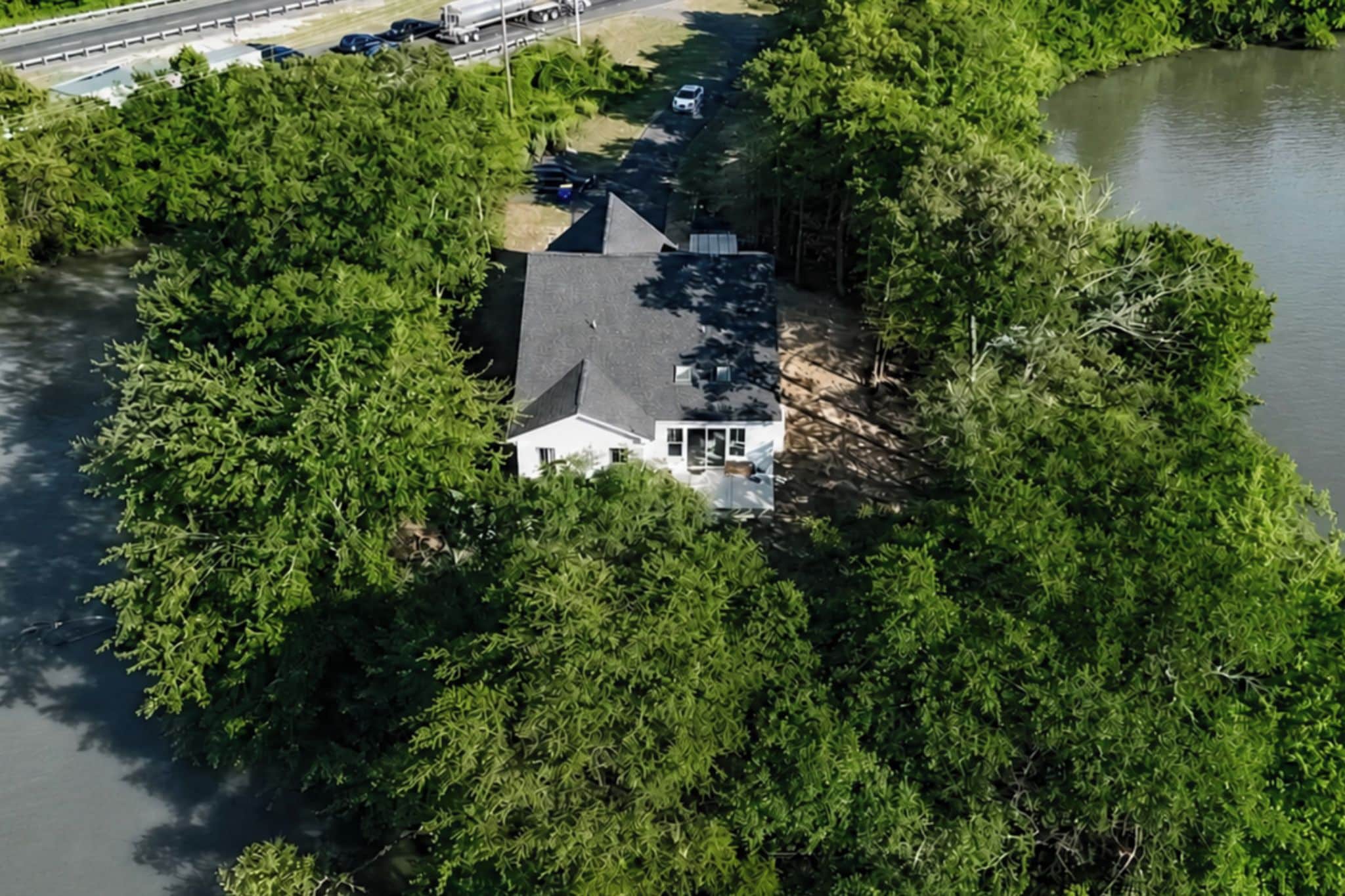 A house surrounded by dense trees, with a body of water nearby.