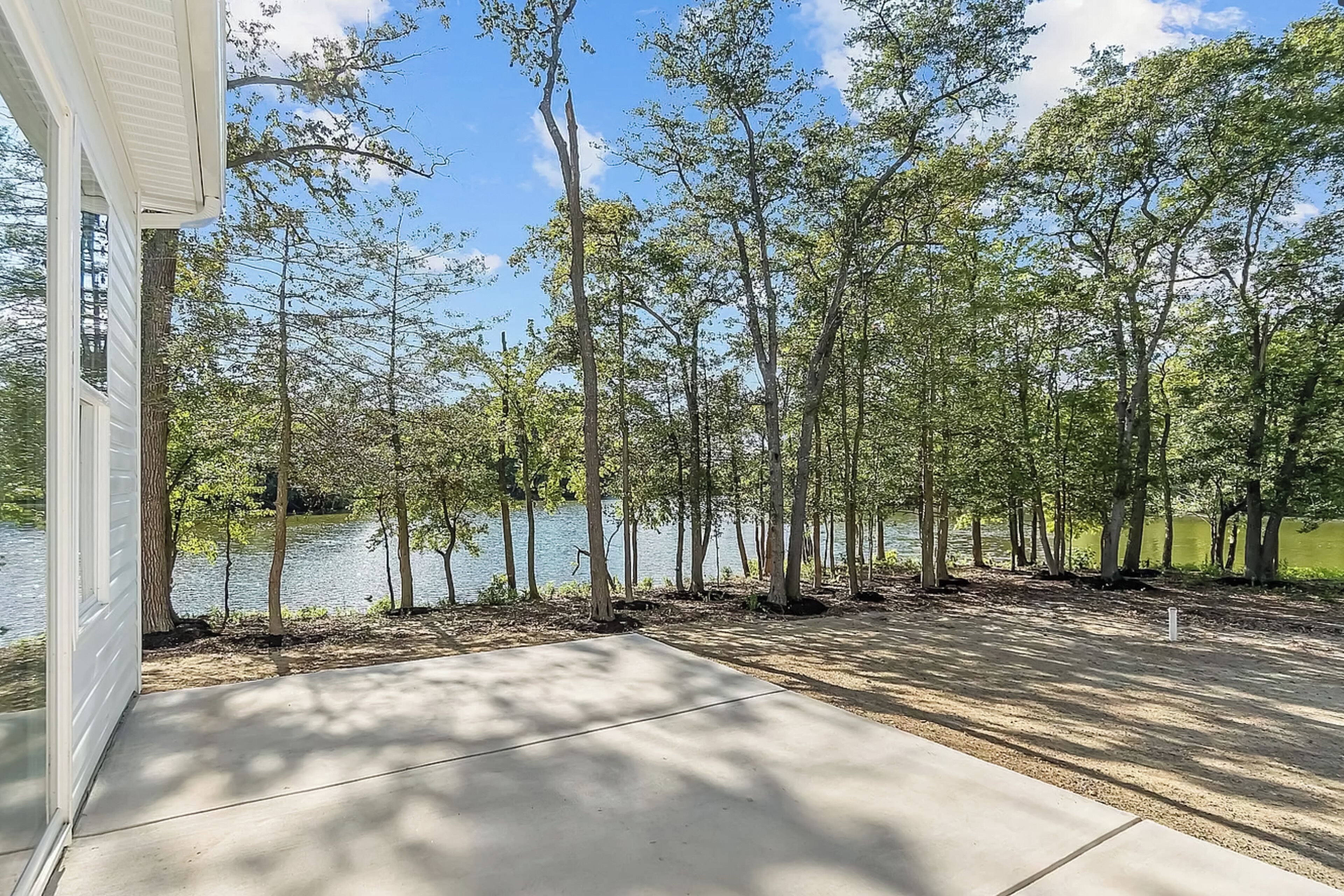 A view of a lakeside property with a concrete patio and tall trees.