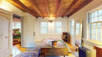 A room with a wooden ceiling, a bed with a patterned bedspread, a potted plant on a wooden bench, and a bookshelf.