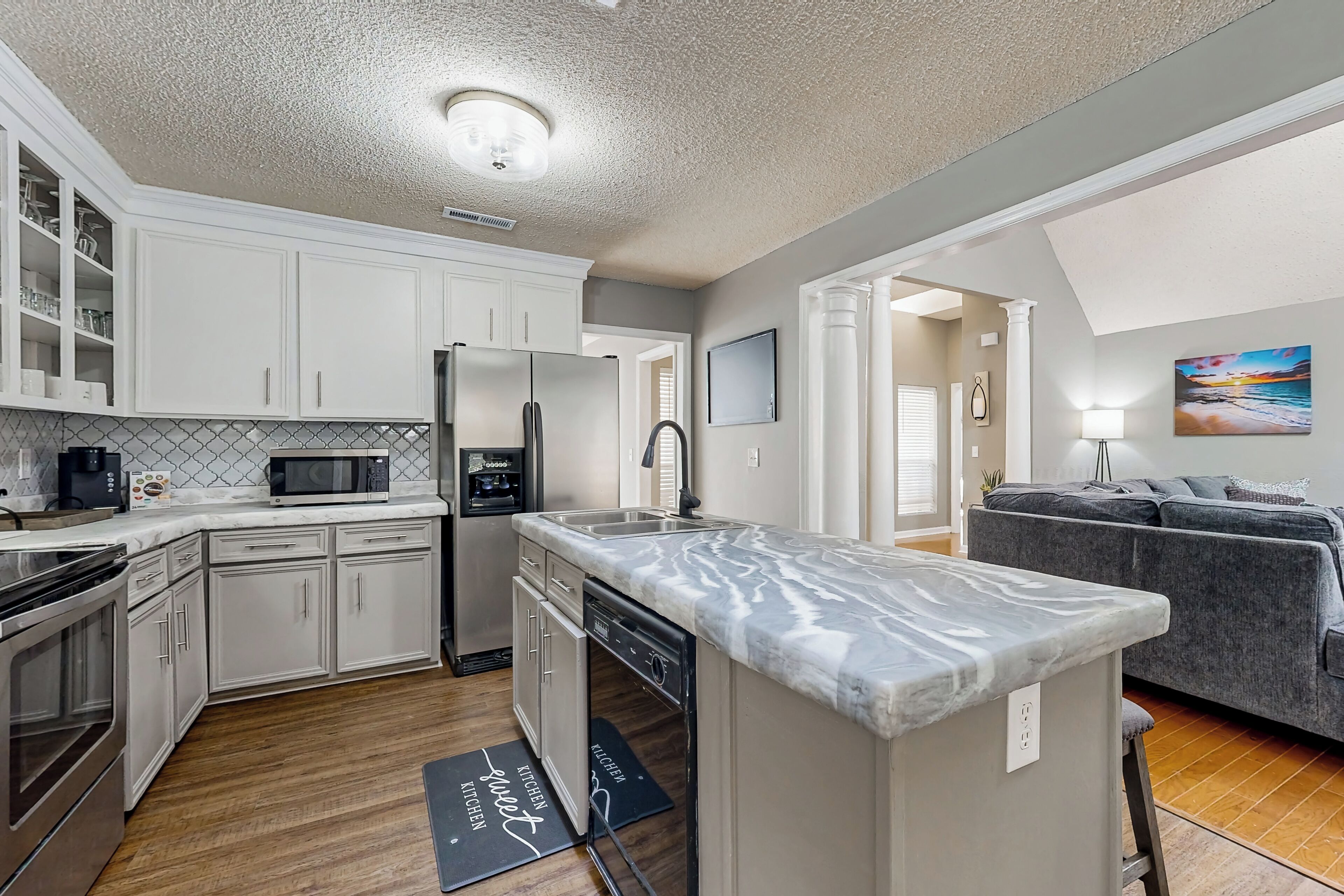 A modern kitchen with white cabinets, a marble countertop, and a built-in dishwasher.