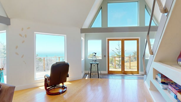 Une pièce spacieuse avec un plafond haut, de grandes fenêtres, un plancher en bois, un fauteuil à bascule, un bureau et une bibliothèque.