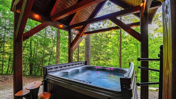 A hot tub under a wooden pavilion with a forest backdrop. - Beautiful Wood Cabin in Red River Gorge (Rogers)