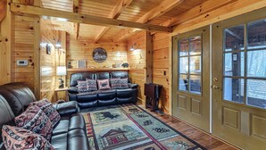 A log cabin interior with a leather sofa, patterned rug, and a wooden door with glass panels. - Beautiful Wood Cabin in Red River Gorge (Rogers)