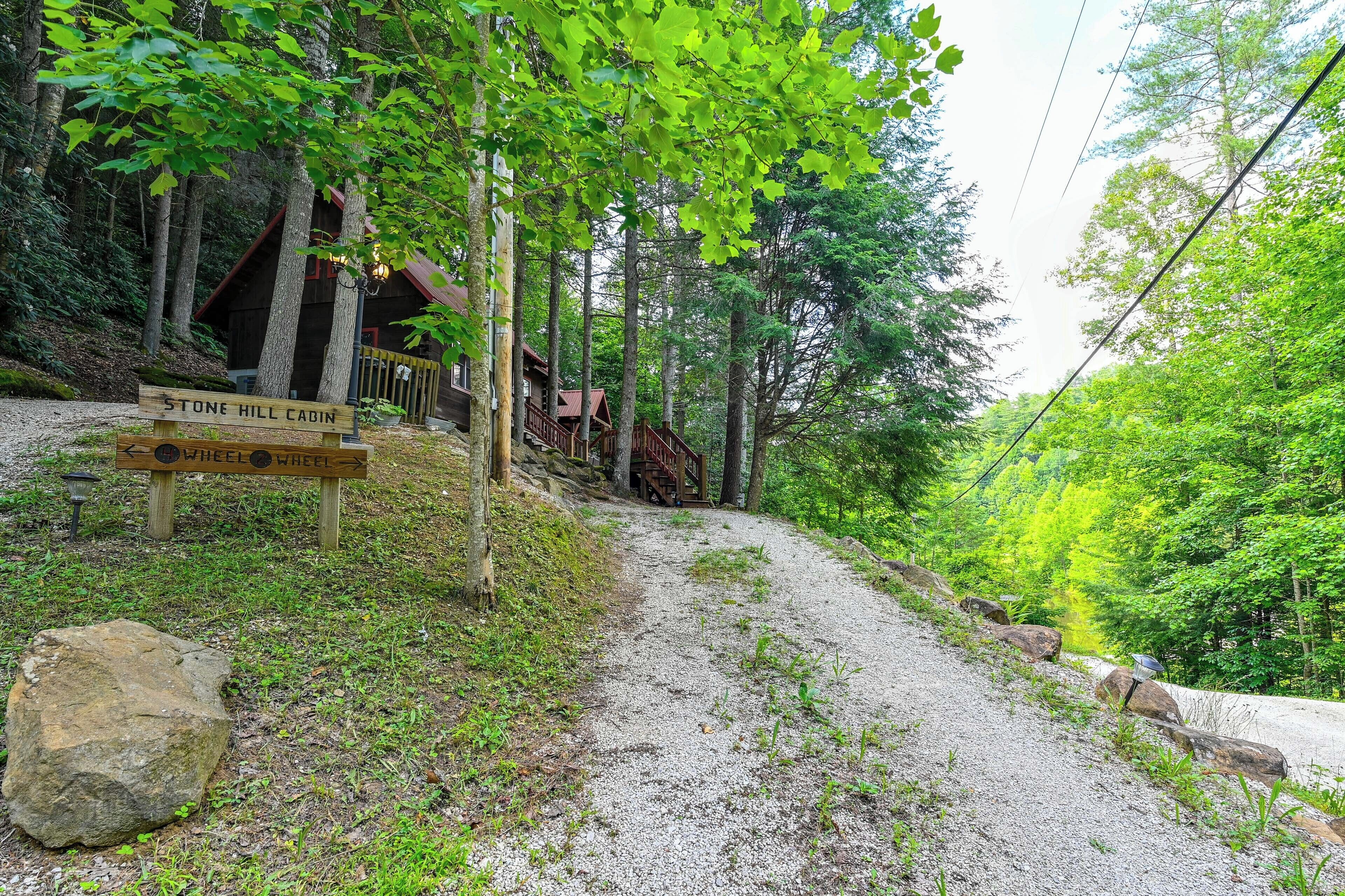 A gravel path leading to a cabin with a sign indicating 'Stone Hill Cabin' and 'Wheel Wheel.'