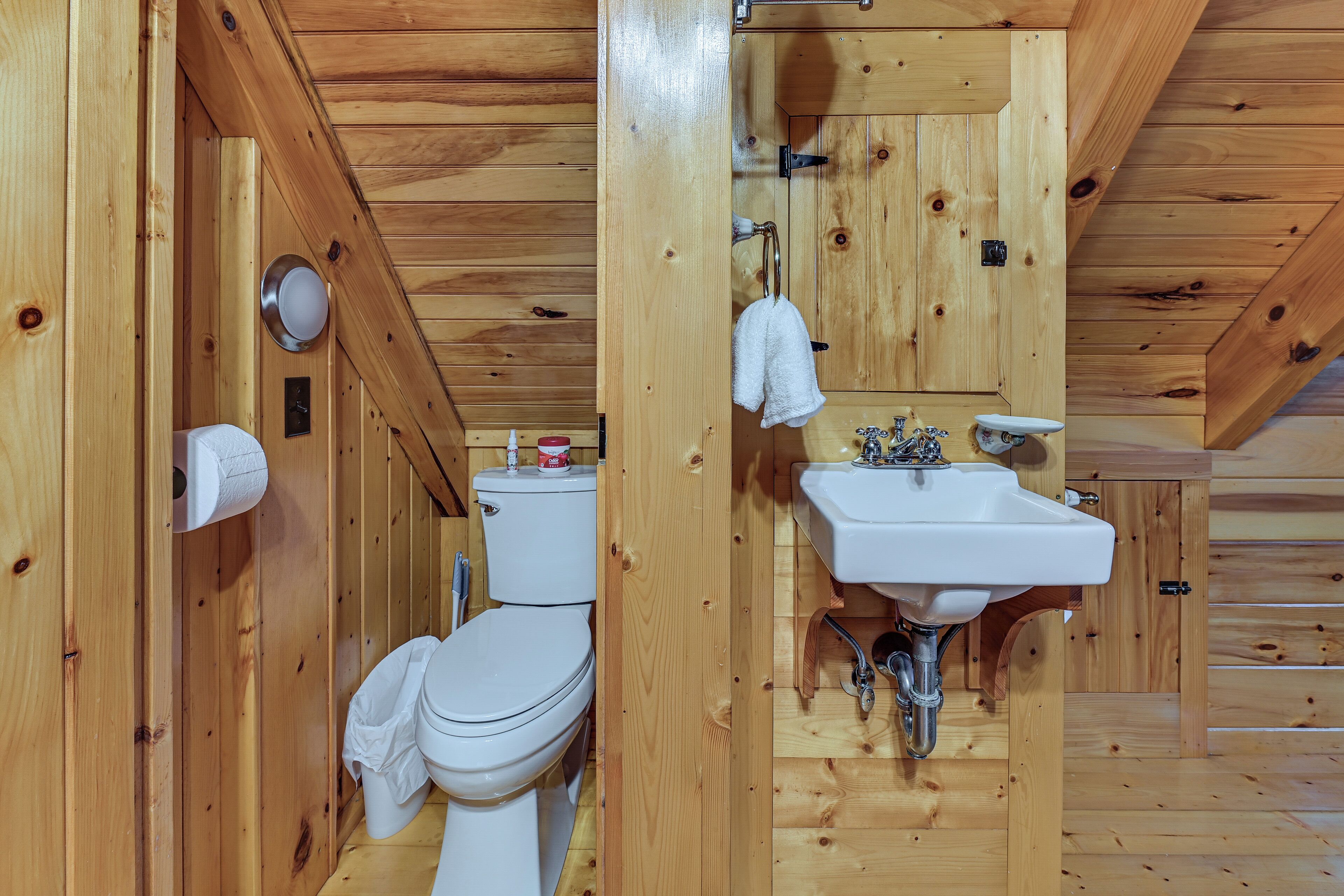 A wooden cabin bathroom with a toilet, sink, and towel hanging on the wall.