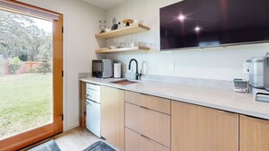 A modern kitchen with wooden cabinets, a built-in microwave, and a large flat-screen TV. - Home w/ Stunning River Views & Nearby Attractions (Myrtle Creek)