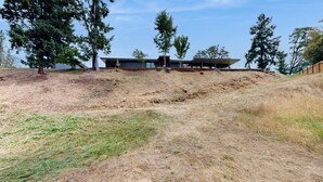 A modern building with a flat roof and large windows, surrounded by trees and a grassy area. - Home w/ Stunning River Views & Nearby Attractions (Myrtle Creek)