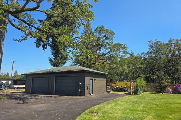 A two-story building with a garage, surrounded by trees and a well-maintained lawn. - Home w/ Stunning River Views & Nearby Attractions (Myrtle Creek)