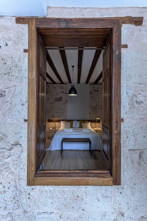 Une petite chambre rustique avec des poutres apparentes, un mur en pierre et un lit simple agrémenté d’une banquette.