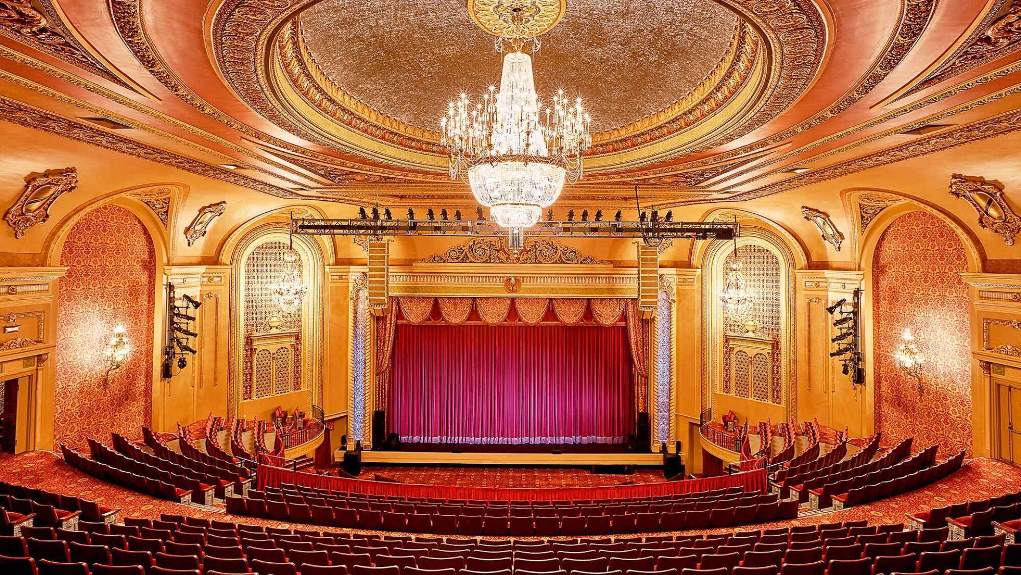 A grand theater with a central stage, ornate ceiling, and rows of red seats.