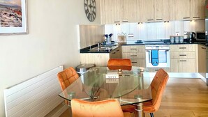 Une cuisine moderne avec des meubles en bois, un four encastré et une table à manger en verre, assortie de chaises orange.