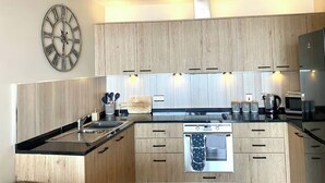 Une cuisine moderne avec des meubles en bois, un évier en acier inoxydable, un four encastré et une horloge murale.